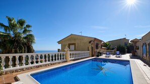 Ein Pool mit Blick auf das Meer, eine weiße Brüstung und ein Gebäude mit einem Ziegeldach.