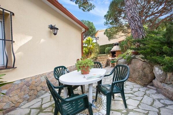 An outdoor patio with a round table and four chairs, surrounded by stone walls and greenery.
