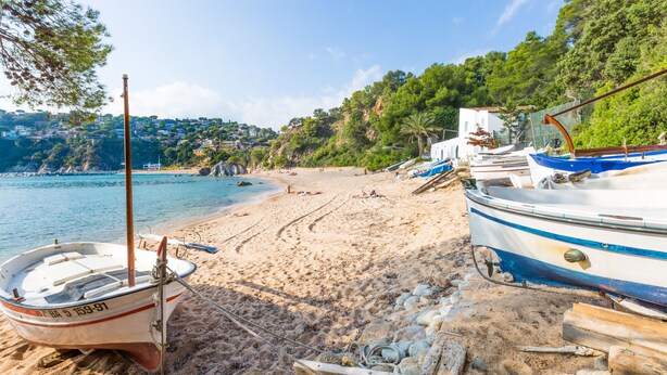 Ein Strand mit Booten, sandigem Ufer und einer bewaldeten Hügelkette im Hintergrund.