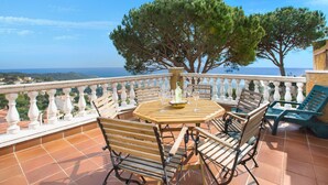 Eine Terrasse mit einem runden Holztisch, vier Holzstühlen und zwei grünen Lounge-Sesseln.