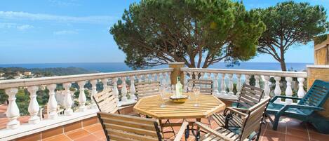 A terrace with a round wooden table, four wooden chairs, and two green lounge chairs.
