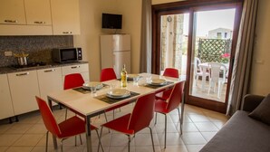 Una cocina moderna con una mesa de comedor para cuatro personas, sillas rojas, un televisor sobre el microondas y una puerta corrediza de vidrio a un patio.
