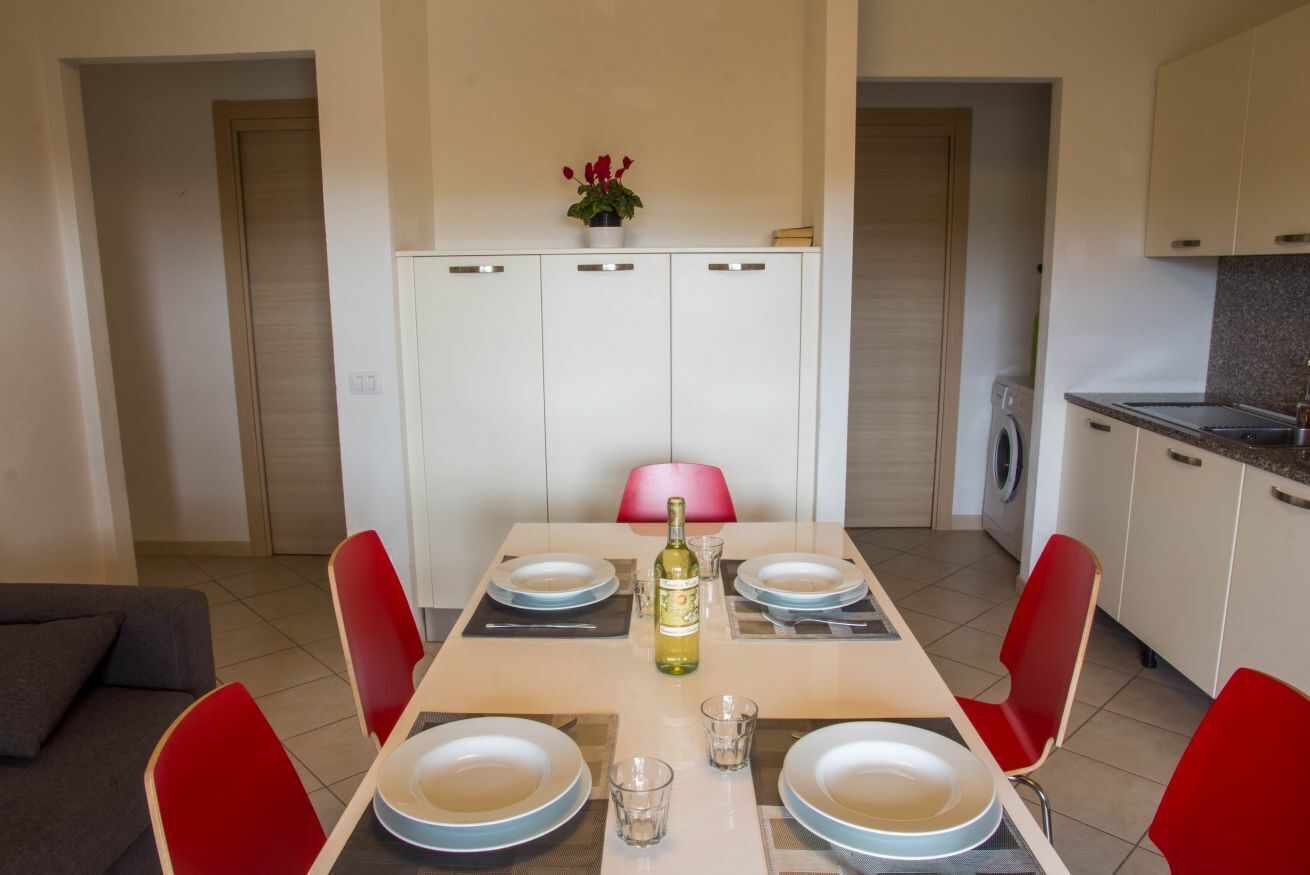A dining area with a table set for four, a bottle of wine, and a potted plant on the wall.