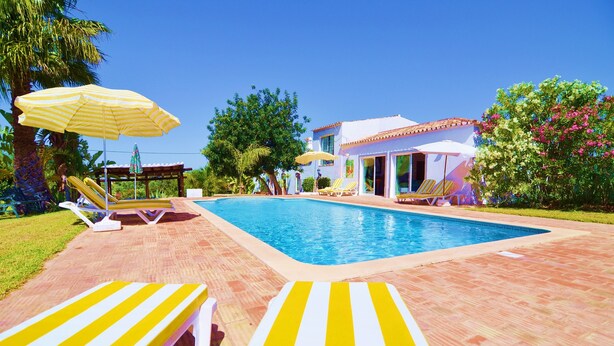 A swimming pool with lounge chairs and umbrellas, surrounded by a patio area and a building with a tiled roof. - Beautiful Restored Algarve Typical Farmhouse, with Private Pool and Sea Views (Loule)
