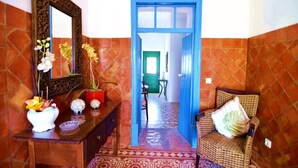 A hallway with a blue door, a wicker chair with a pillow, a mirror, and a table with decorative items. - Beautiful Restored Algarve Typical Farmhouse, with Private Pool and Sea Views (Loule)