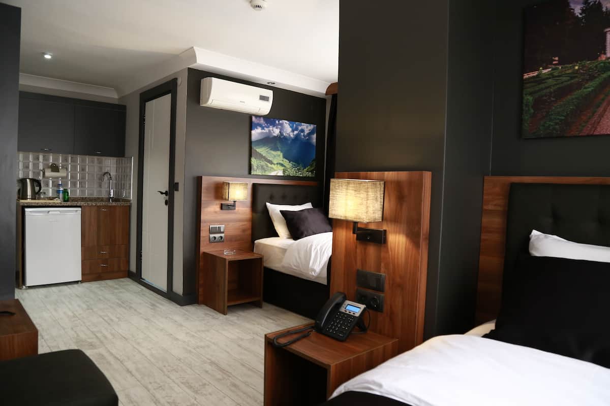 Ein kleines Hotelzimmer mit Küchenzeile, einem Bett mit Kopfteil, Nachttischen, einem Telefon und einer Wand-Klimaanlage.