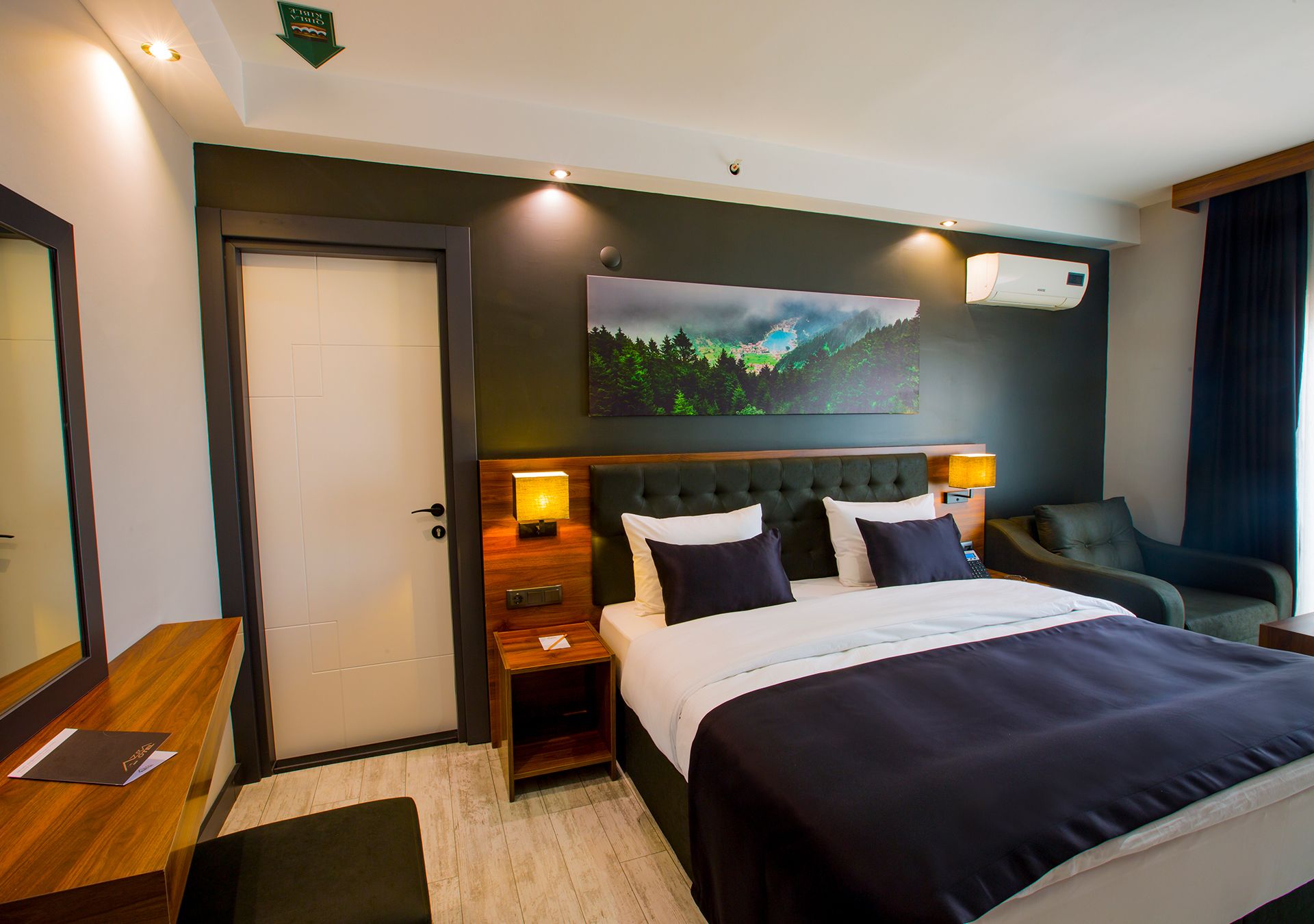 Hotelkamer met een bed, nachtkastjes, een bureau, een stoel, een schilderij en een airconditioning.