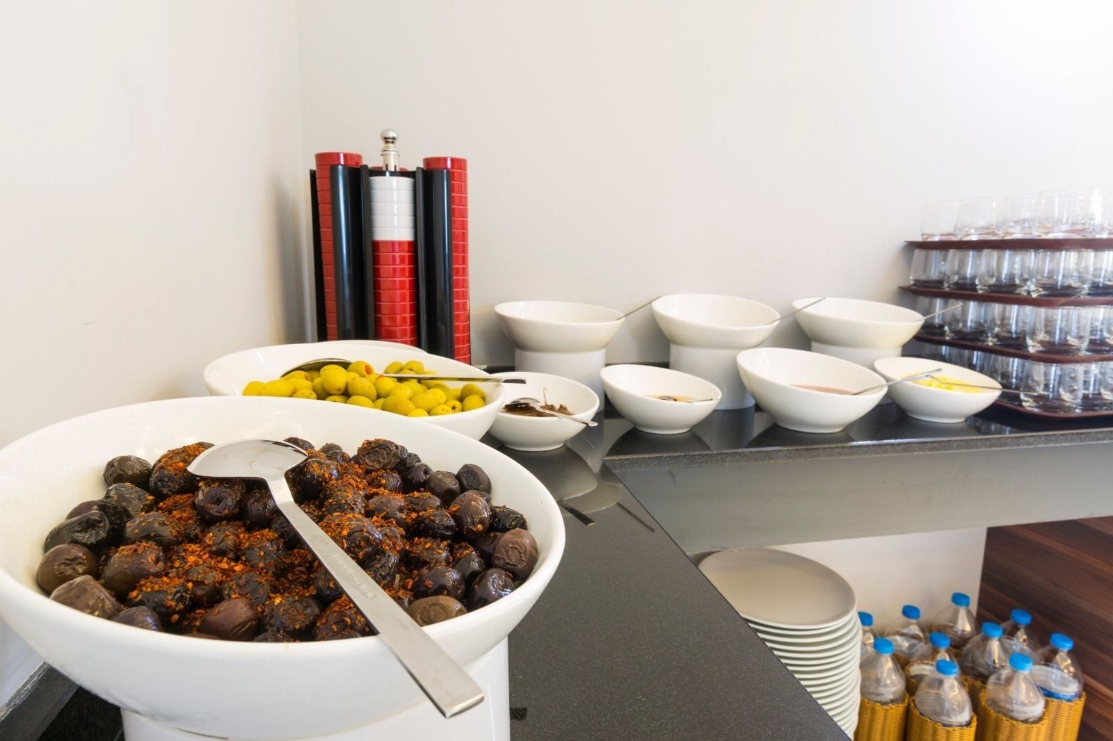 Montaje tipo bufé con diversos alimentos, incluyendo aceitunas y limones, y múltiples tazones y vasos.