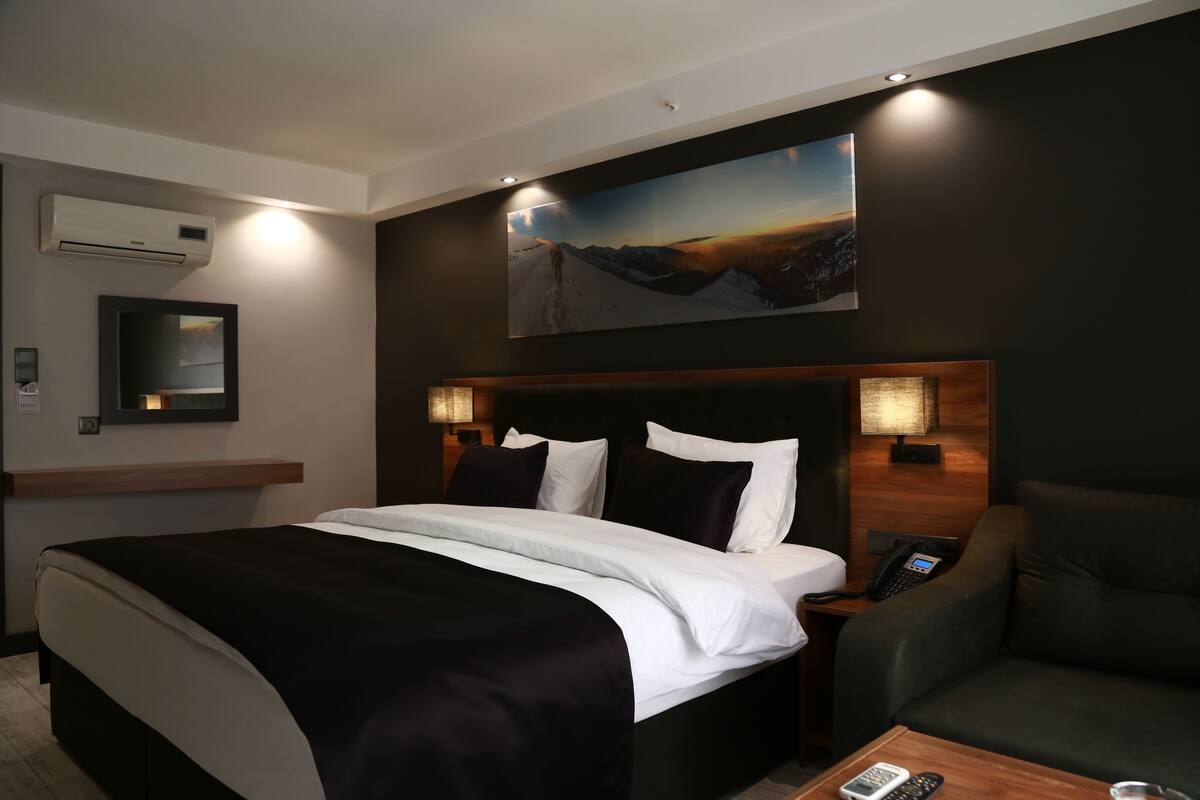 Ein Hotelzimmer mit einem großen Bett, einem Schreibtisch, einem Sessel, einem Bild und einem an der Wand befestigten Telefon.