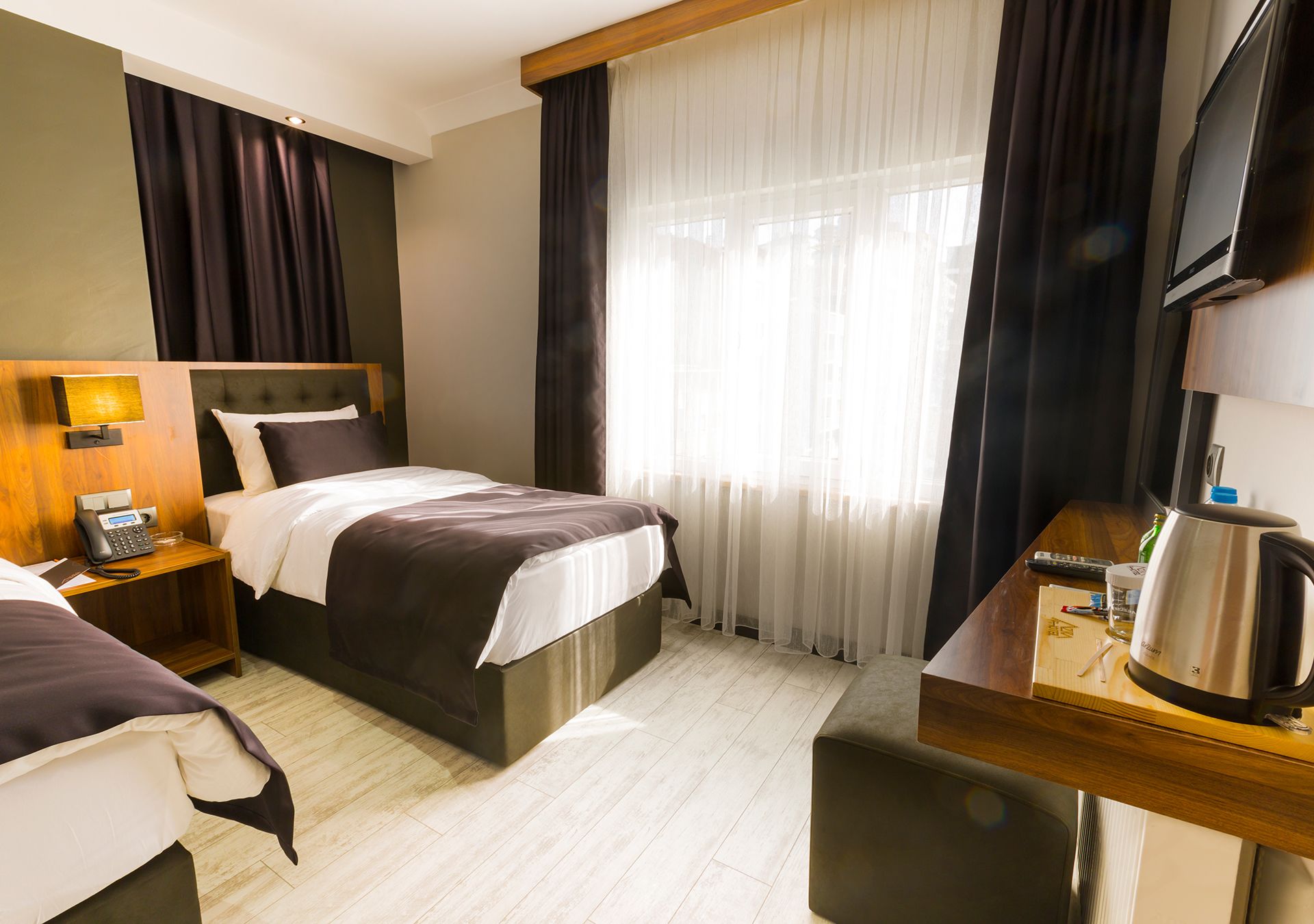A hotel room with two beds, a desk with a coffee maker, a TV, and a telephone on the nightstand.