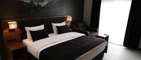 Ett modernt hotellrum med en stor säng, två sängbord med lampor, en sänggavel, en tavla på väggen och ett fönster med gardiner.