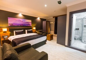 A modern hotel room with a large bed, a sofa, a desk, and a bathroom with a glass shower. - Azra Suite Otel (Trabzon)