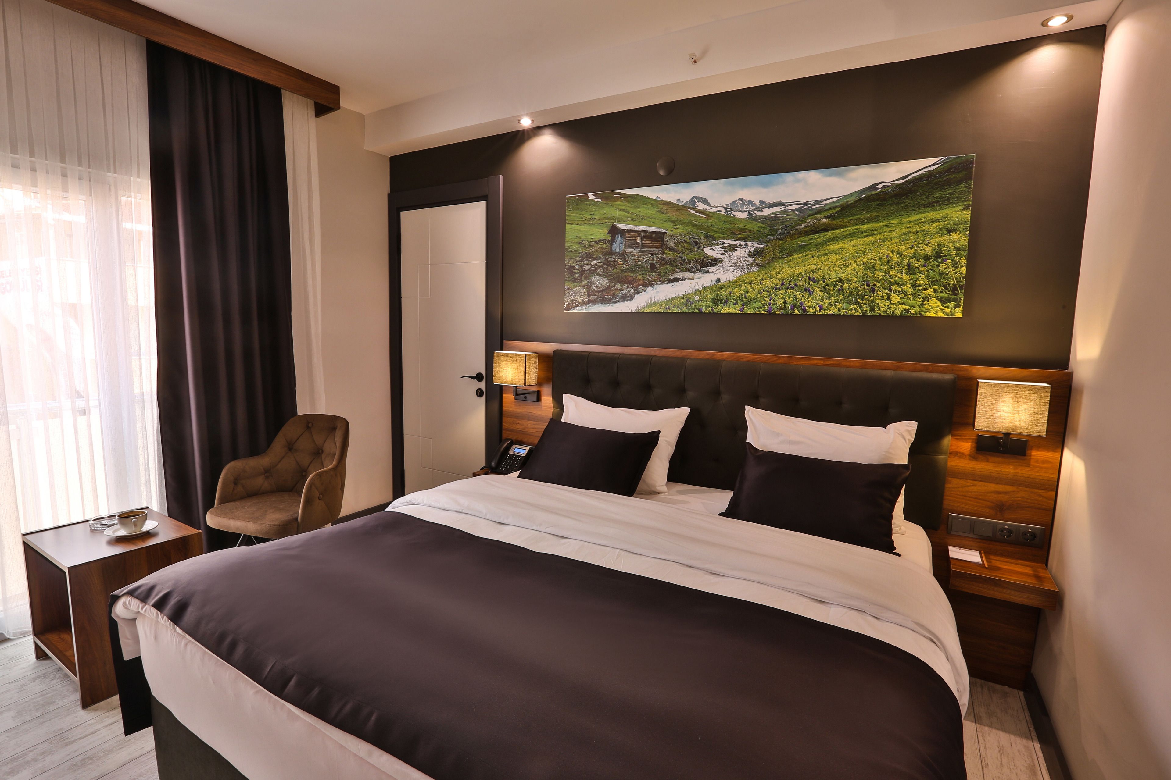 A hotel room with a large bed, a chair, a bedside table, a lamp, and a painting on the wall.