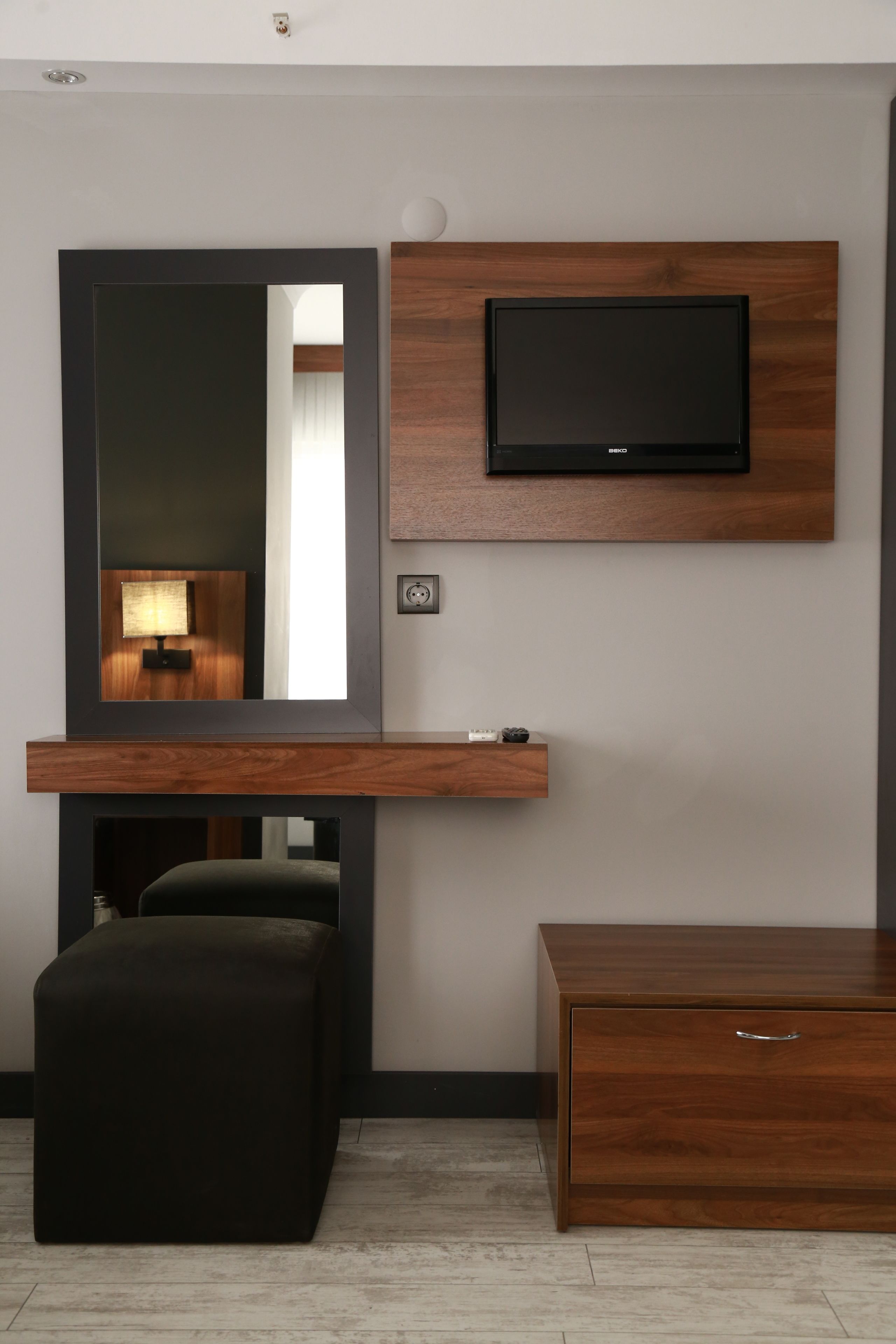 A modern room with a wooden TV stand, a large mirror, a small table, and a dark ottoman.