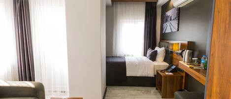 Quarto de hotel com cama, escrivaninha com telefone, mesinha com frutas e ar-condicionado fixado na parede.