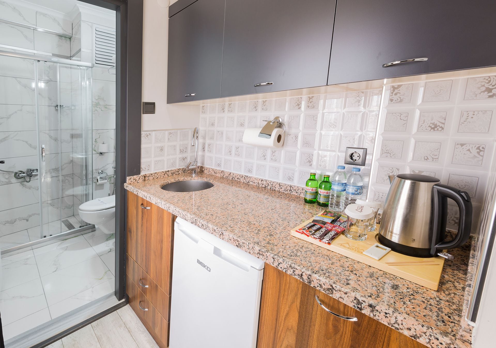 A modern kitchen with granite countertops, a dishwasher, a coffee maker, and a glass shower enclosure.