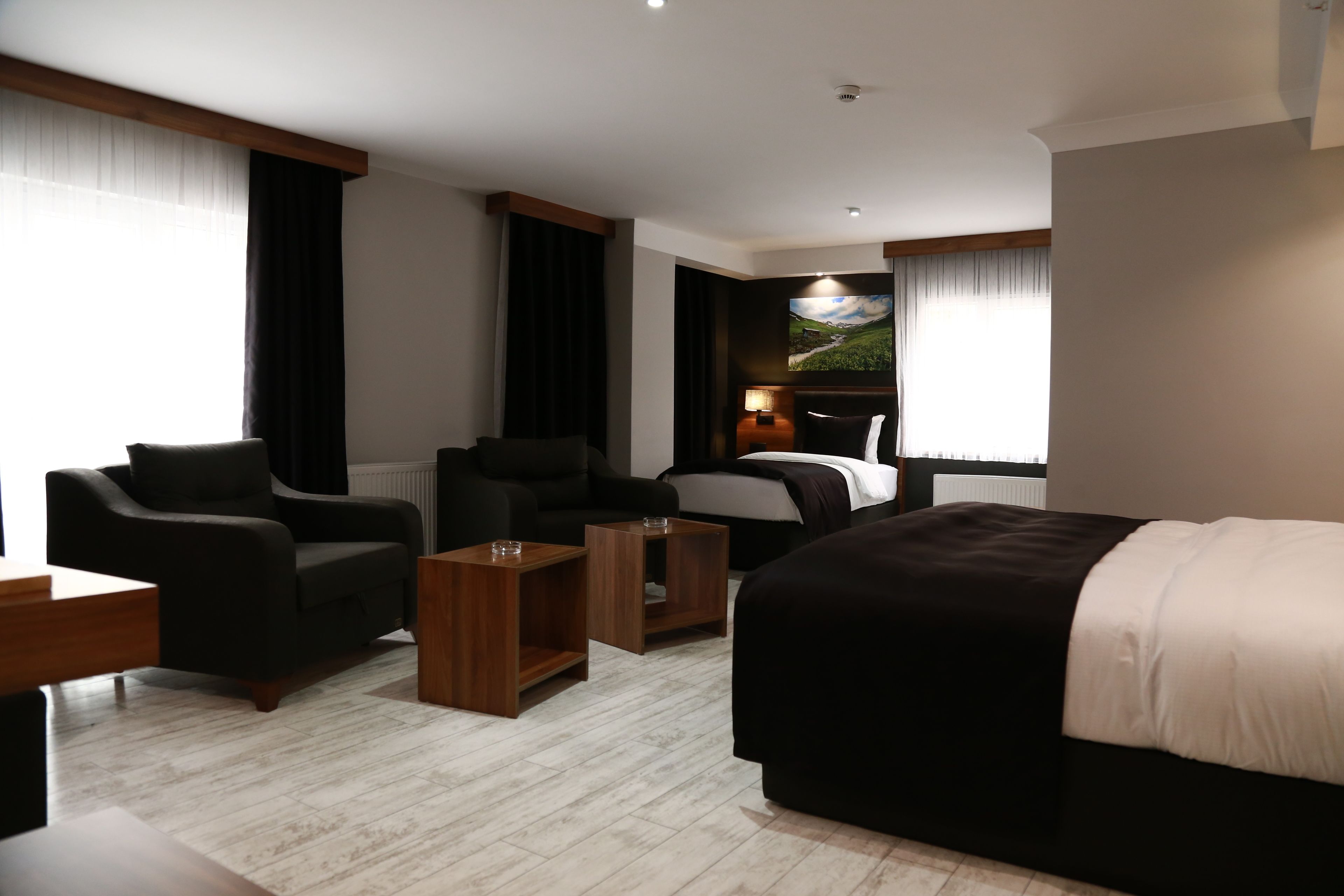 A modern hotel room with a large bed, two armchairs, a wooden coffee table, and a view of a mountainous landscape through the window.