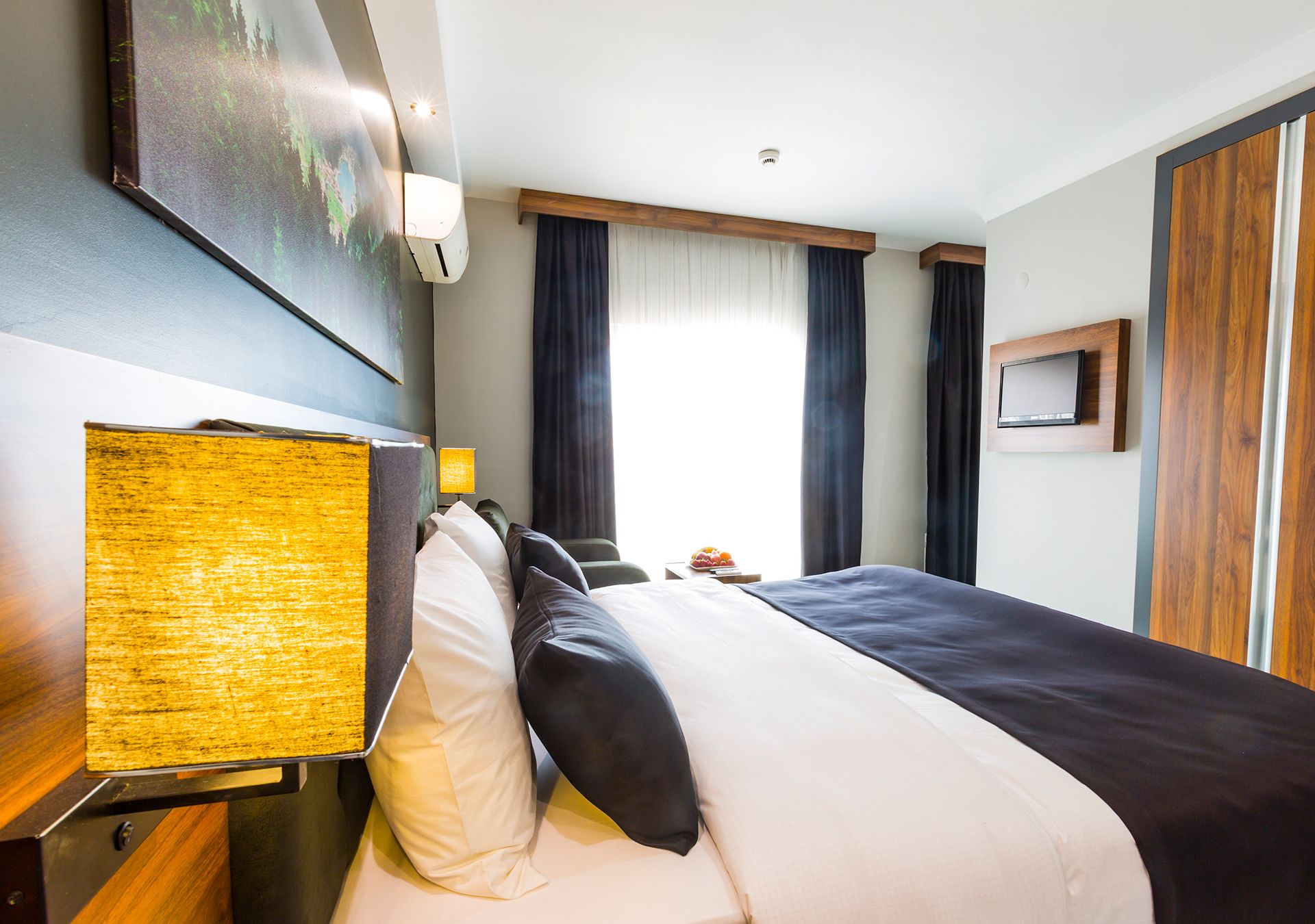 A hotel room with a large bed, a mounted TV, and a painting on the wall.