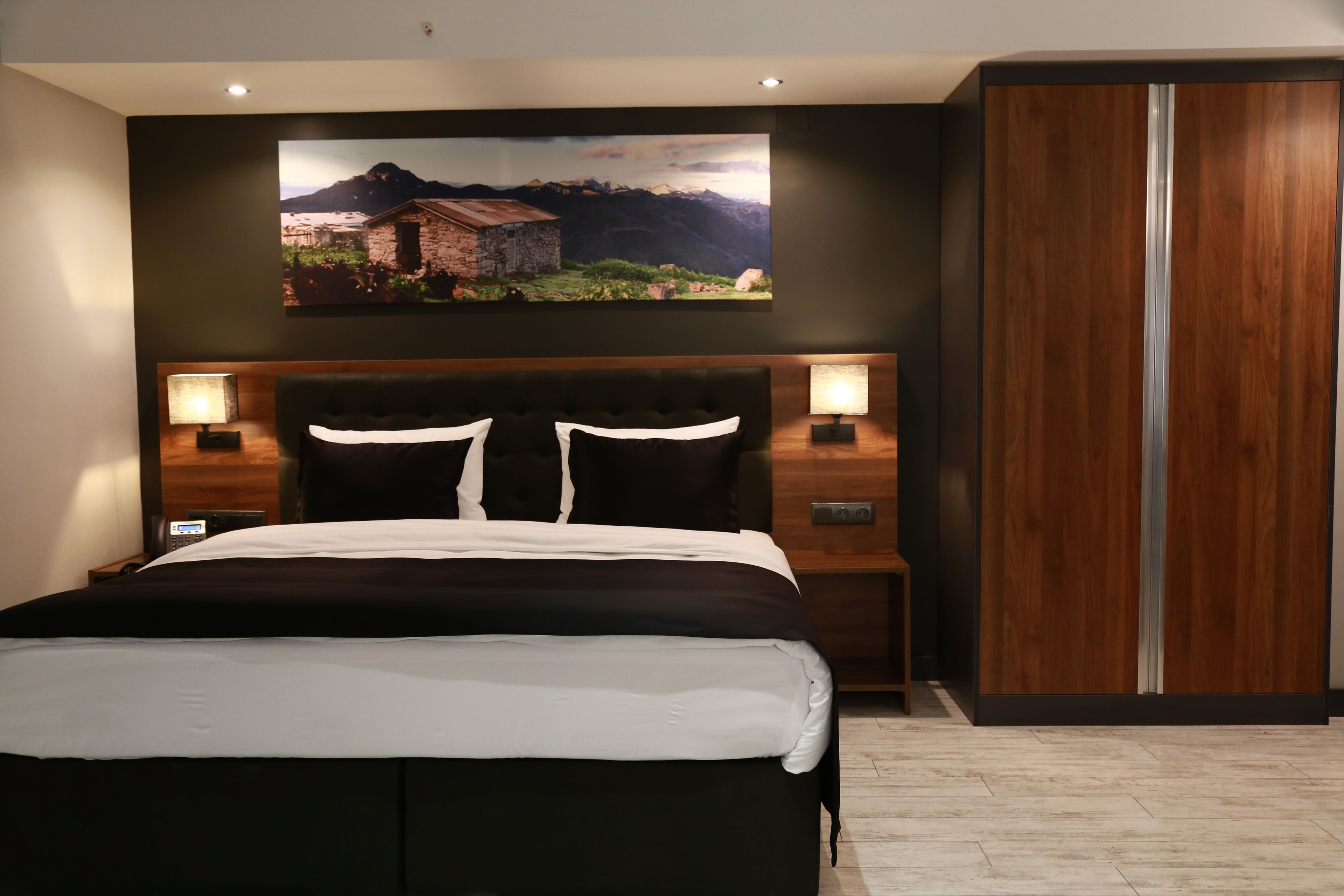 Un dormitorio moderno con una cama grande, cabecera de madera, dos mesitas de noche con lámparas y un armario.
