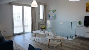 A modern living room with a glass partition, a dining area with a white table and chairs, and a large window with curtains. - PENTHOUSE MARIS ALGHERO VIALE SARDINIA 104 LUXURY PENTHOUSE NEAR THE BEACH (Alghero)