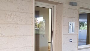 A corridor with a glass door leading to a room, tiled floor, and a wall-mounted light fixture. - PENTHOUSE MARIS ALGHERO VIALE SARDINIA 104 LUXURY PENTHOUSE NEAR THE BEACH (Alghero)