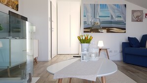 A modern living room with a white table, a blue sofa, and a painting of a beach scene. - PENTHOUSE MARIS ALGHERO VIALE SARDINIA 104 LUXURY PENTHOUSE NEAR THE BEACH (Alghero)
