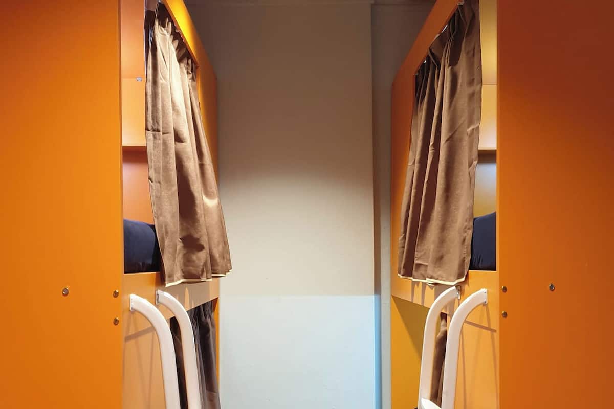 A narrow corridor with bunk beds, each with a curtain and a ladder.