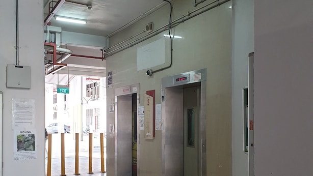 A corridor with tiled flooring, an exit sign, and an elevator. - Century Service World - Hostel (Singapore)