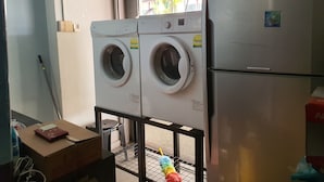 A laundry room with two front-loading washing machines and a refrigerator. - Century Service World - Hostel (Singapore)