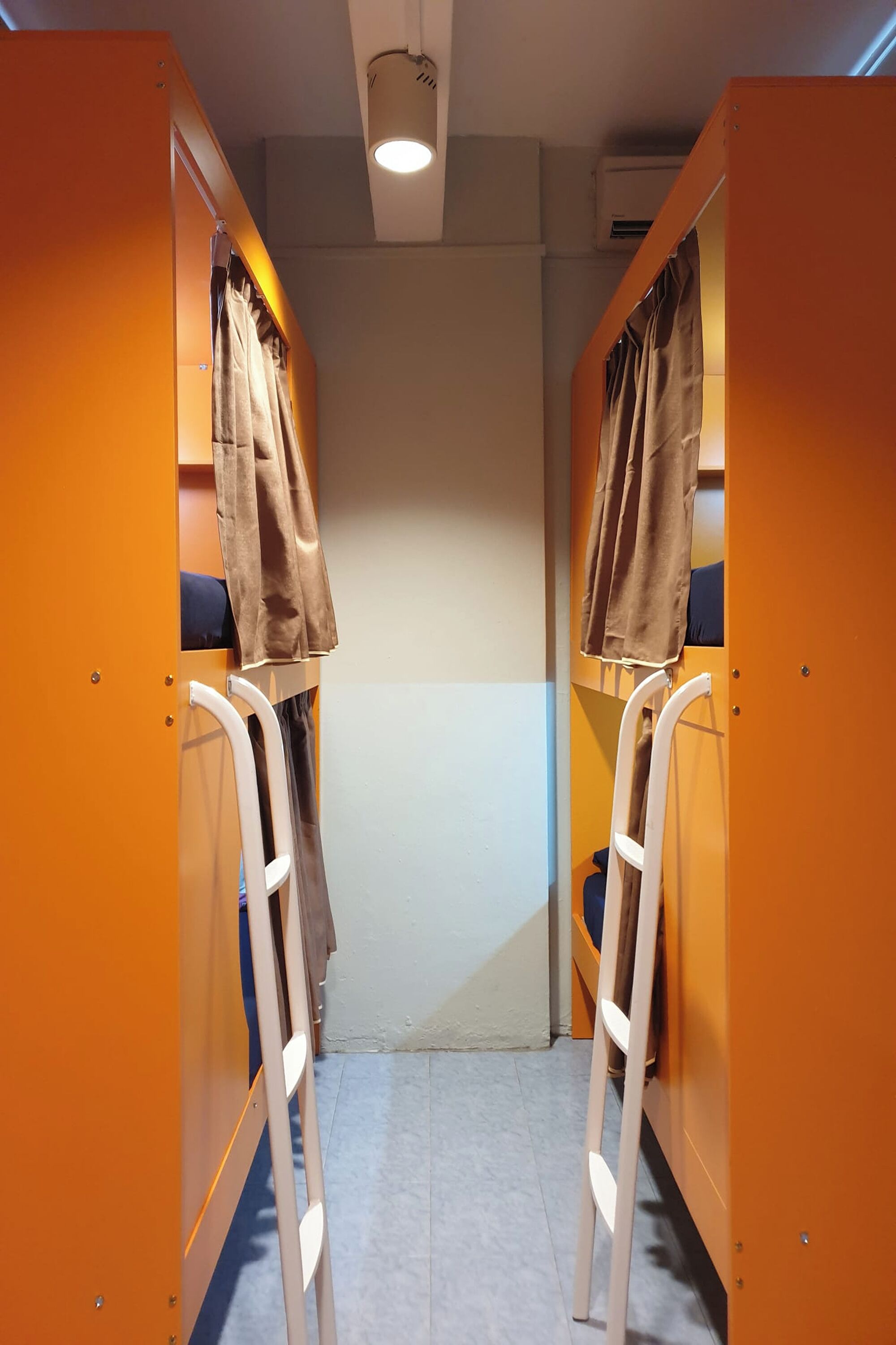 A narrow corridor with bunk beds, each with a curtain and a ladder.