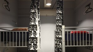 A dormitory room with bunk beds, a hanging light fixture, and a curtain with a black and white pattern. - Century Service World - Hostel (Singapore)