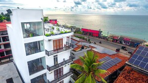 A multi-story building with balconies, solar panels on the roof, and a view of the sea. - Rominrich (Hikkaduwa)