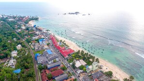 An aerial view of a coastal town with a beach, boats, and a mix of residential and commercial buildings. - Rominrich (Hikkaduwa)