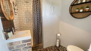 Ein Badezimmer mit Dusche, Toilette, Waschbecken, Spiegel, einem gemusterten Duschvorhang, einem Wanddekor und einem Regal mit kleinen Pflanzen.