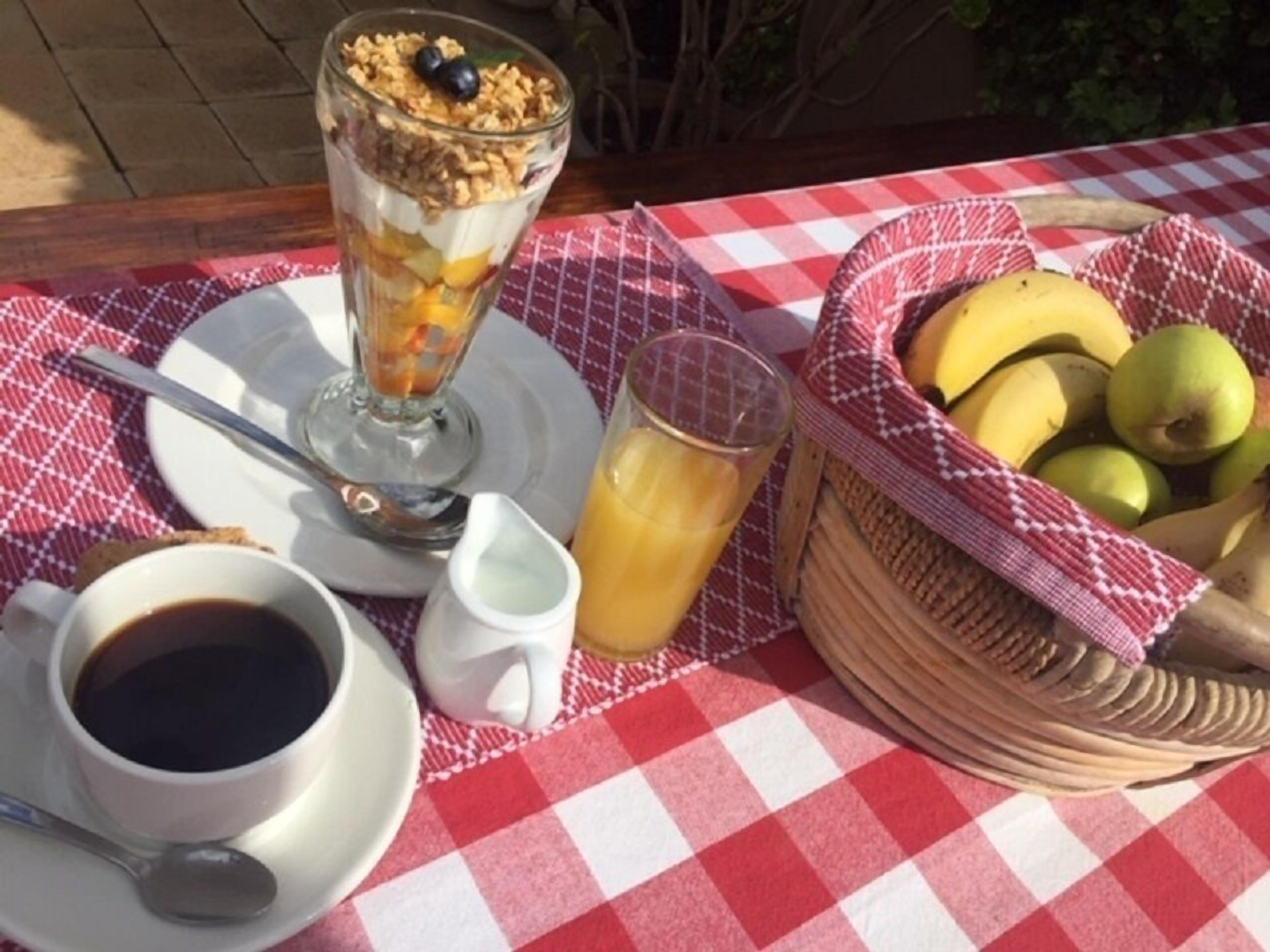 A breakfast setting with a checkered tablecloth, a fruit basket, a glass of juice, a cup of coffee, and a dessert.