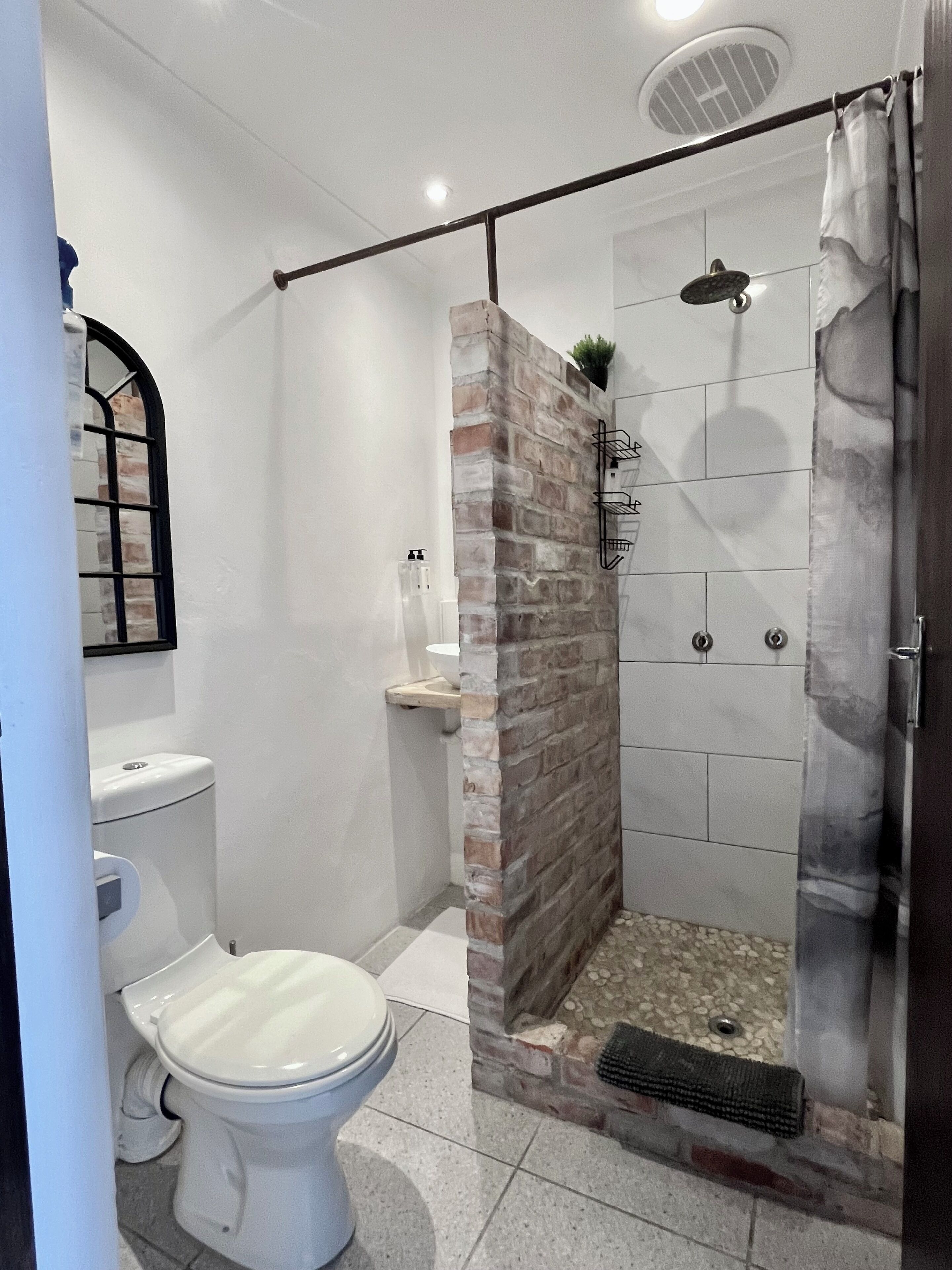 Un baño con inodoro, ducha con puerta de cristal y pared decorativa de ladrillo.