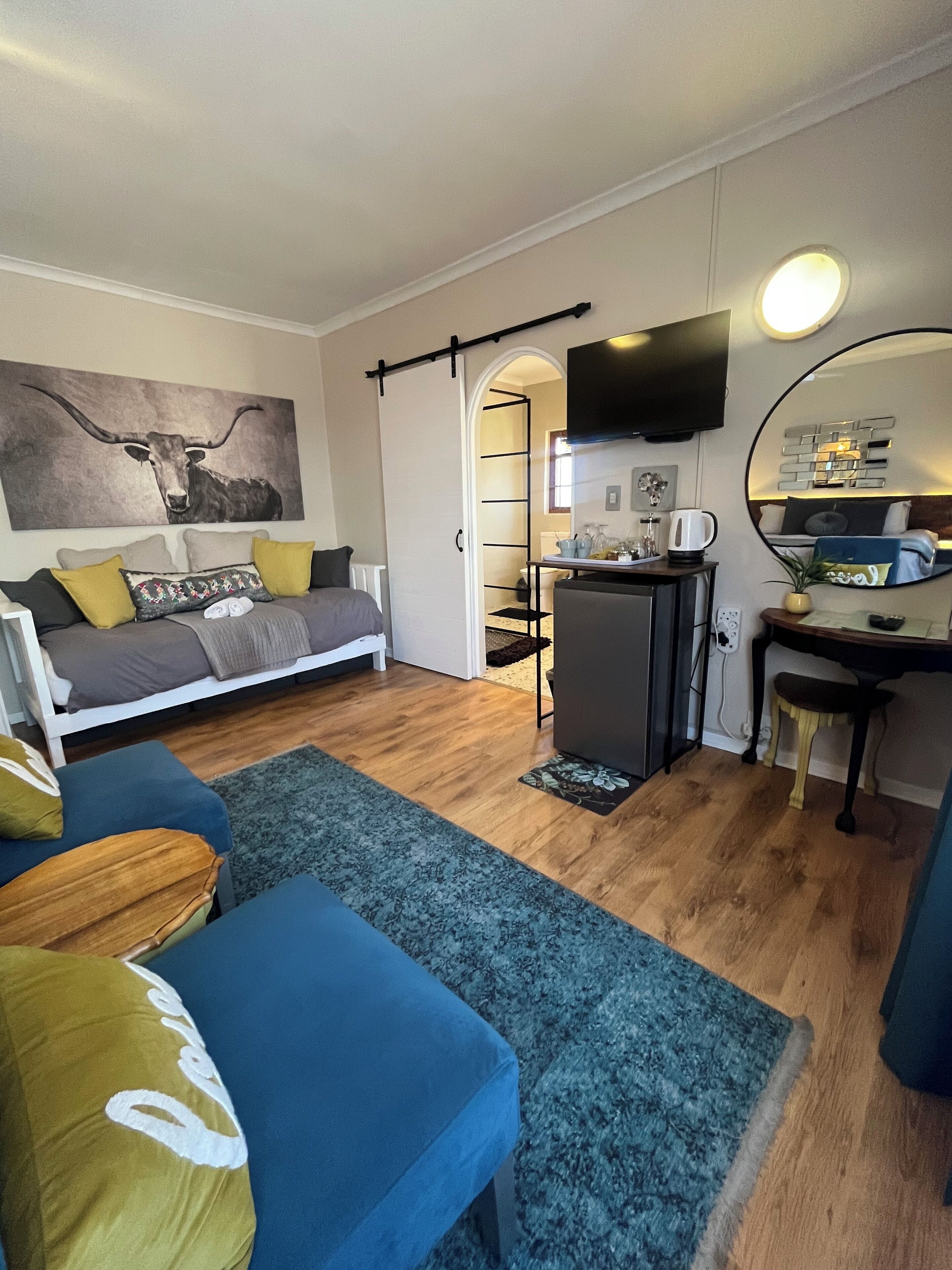Un espace de vie compact comprenant un canapé, une petite table à manger, un téléviseur fixé au mur et un coin cuisine.