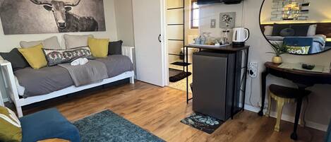 Un espace de vie compact comprenant un canapé, une petite table à manger, un téléviseur fixé au mur et un coin cuisine.