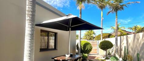 Un patio con mesa y bancos de madera, rodeado de palmeras y un jardín de cactus.