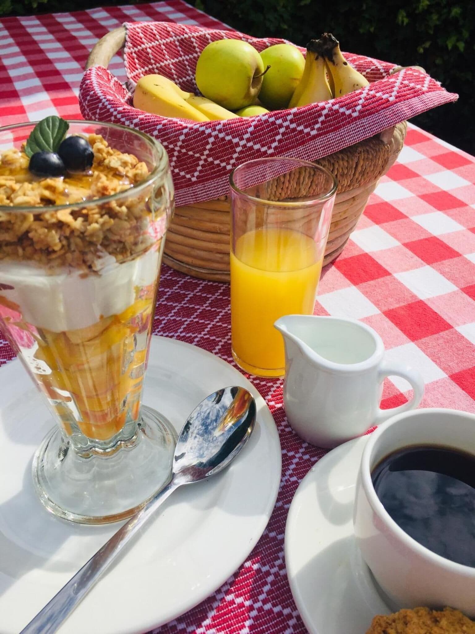 Un esmorzar amb un dolç en un vas, un got de suc d'aranja, una cistella de fruita i una tassa de cafè sobre una tela escamotada.