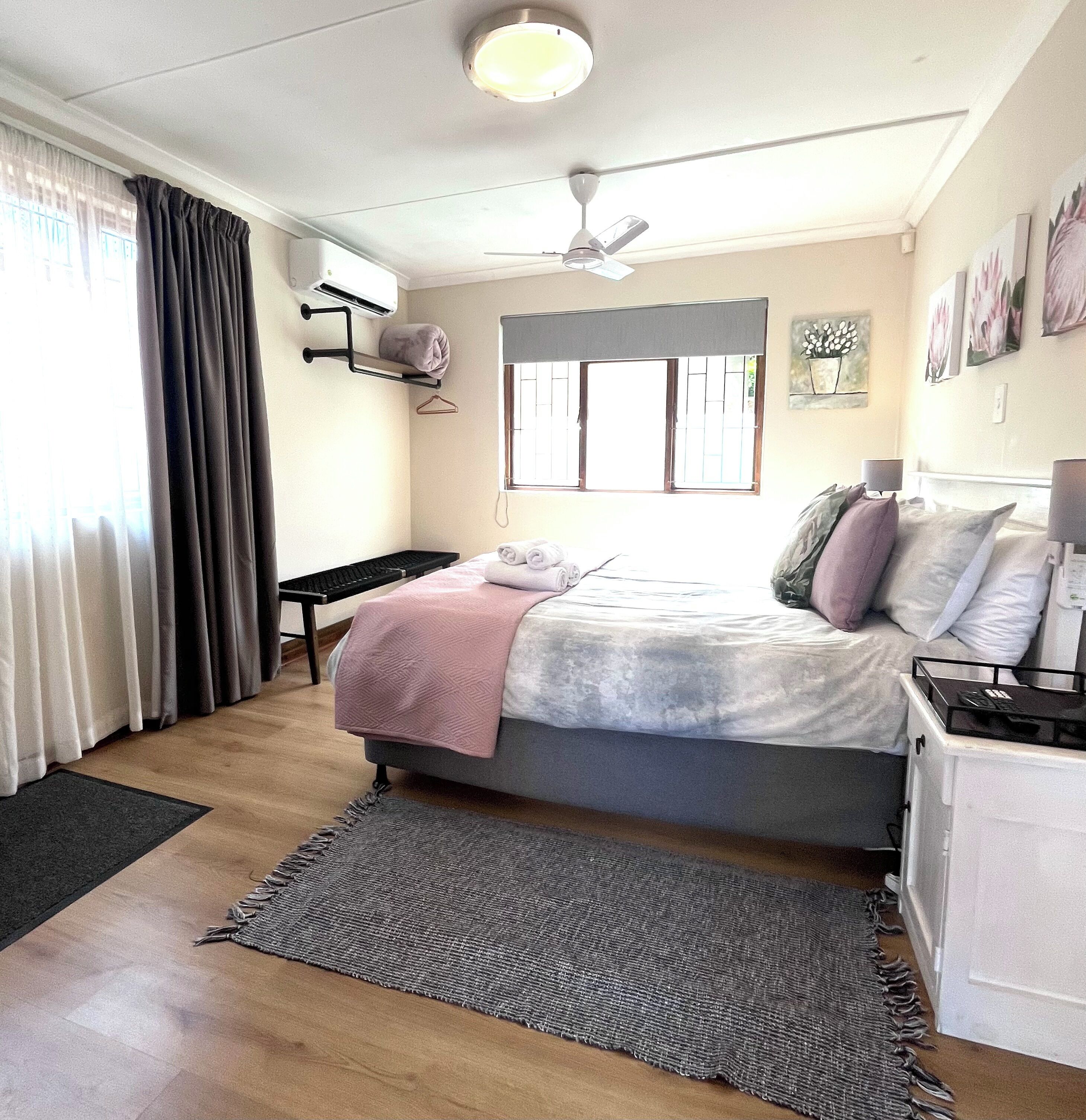A bedroom with a bed, bedside tables, a ceiling fan, a window with curtains, and wall art.
