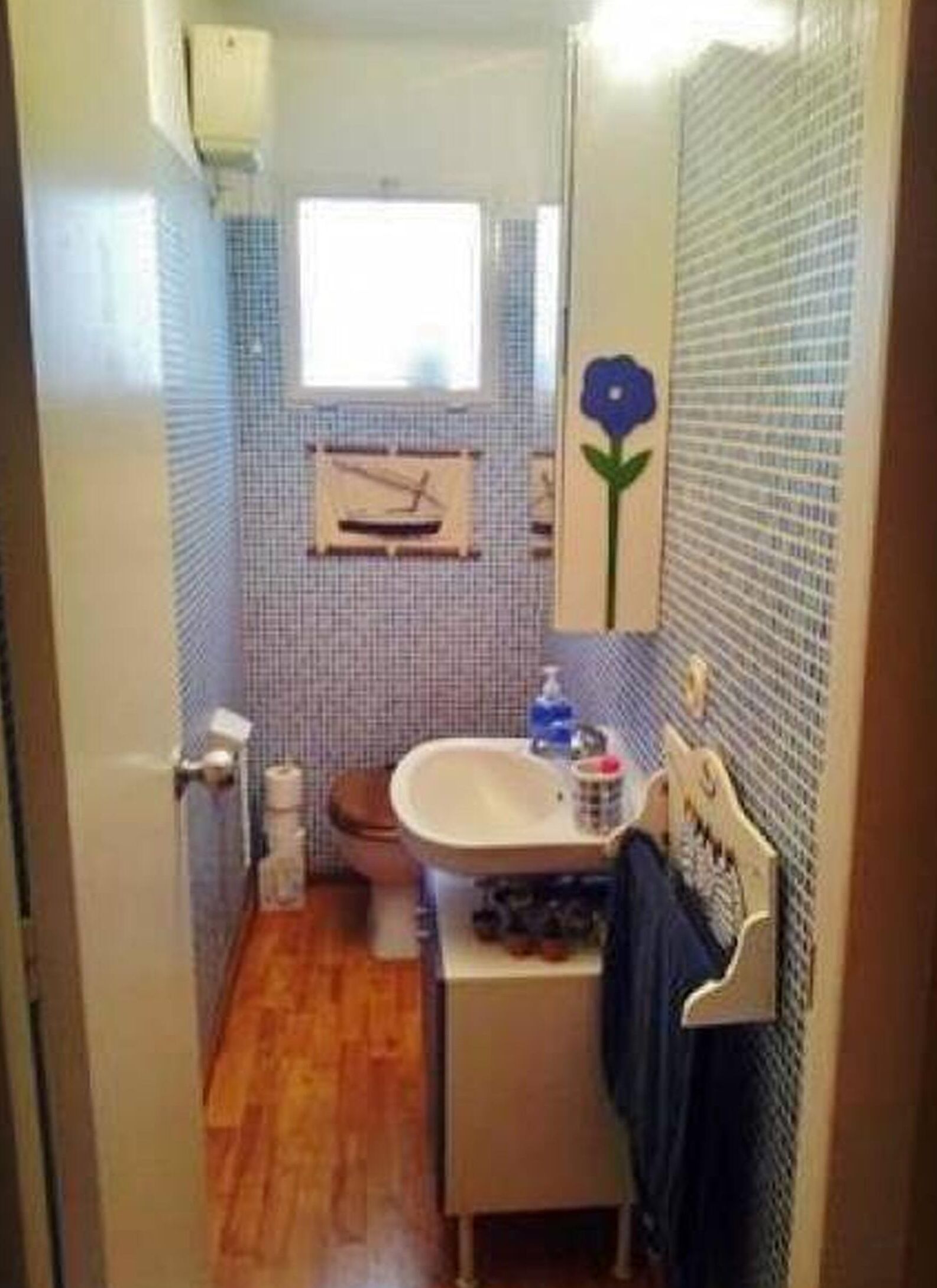 Un bagno piccolo con pavimento in legno, un water, un lavandino con specchio e una finestra sopra il water.