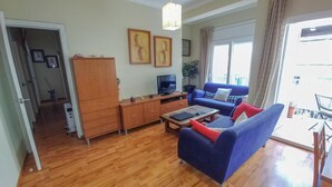 A living room with a sofa, coffee table, TV, and wooden cabinet. There is a door leading to another room and a window with curtains. - Family Apartment Just Steps from the Sea in Palamós 🏖️☀️ (Palamós)