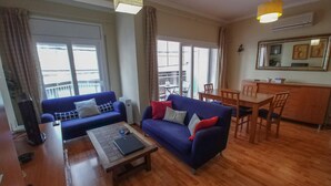 A living room with a blue sofa, a wooden coffee table, and a dining area with a wooden table and chairs. - Family Apartment Just Steps from the Sea in Palamós 🏖️☀️ (Palamós)