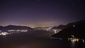 A nighttime view of a coastal town with a starry sky, a calm sea, and distant city lights.