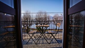 A balcony with a table and chairs, a view of a body of water, and bare trees.