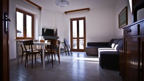 A spacious living area with a dining table, chairs, a sofa, and a television.