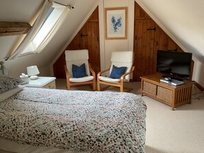 A bedroom with a bed, two chairs, a TV, and a bedside table.