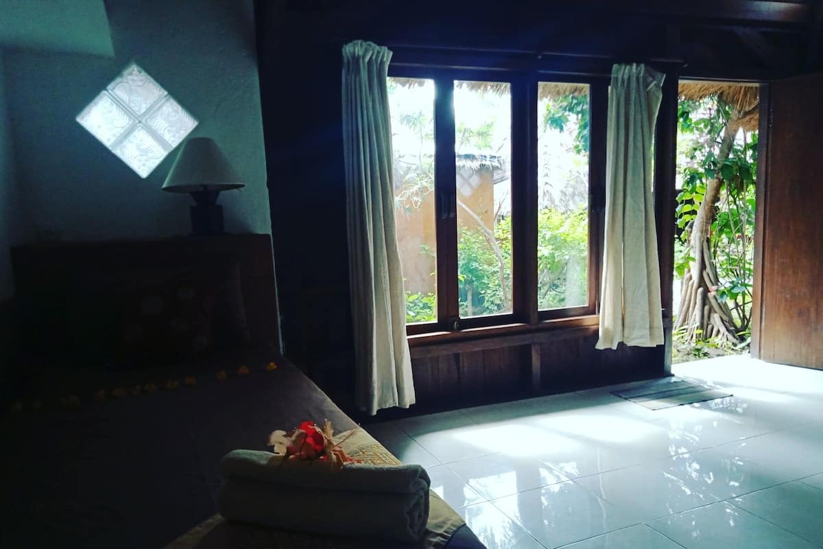 A room with a bed, a window with curtains, and a view of greenery outside.