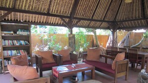 A covered outdoor seating area with wooden furniture, a bookshelf, and a thatched roof. - Gili Hideaway (Gili Trawangan)